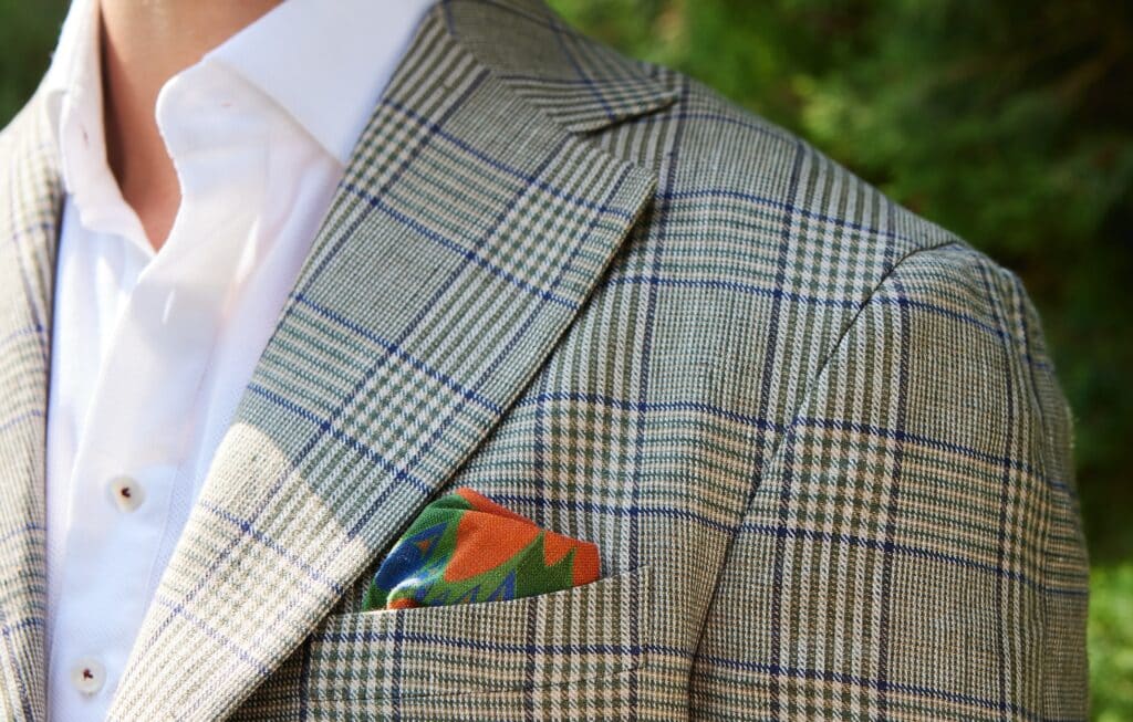 A mid-weight linen suit jacket with a glen plaid with windowpane overcheck in a bold touch of purple (OP2626 Gallipolli), paired with our Quadro OP809 Royal Bird pocket square.